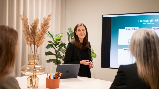 Ung kvinna som står framför skärm i ett konferensrum.