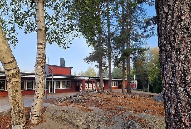 Åvikenskolan. Röd träbyggnad omgiven av träd och stora stenar.