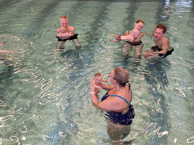 En kvinna instruerar föräldrar som håller i sina bebisar i en bassäng när det är lektion i babysim.