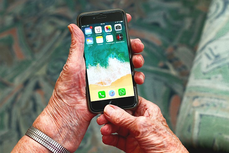 Händer på en äldre person håller i en mobiltelefon.