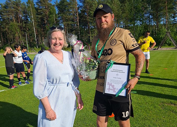 En kvinna och en man, mannen håller i en blomsterbukett och ett diplom.