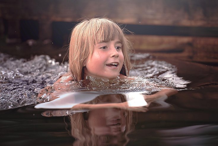 En glad flicka som simmar i en sjö.
