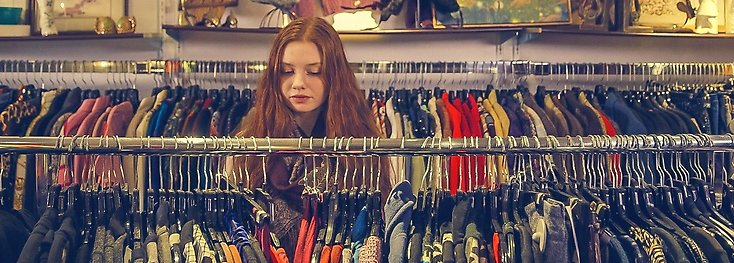En ung kvinna är på en secondhandbutik och letar bland kläder.