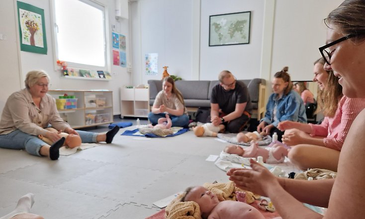 Föräldrar sitter i en ring på golvet med sina babysar på filtar framför sig.