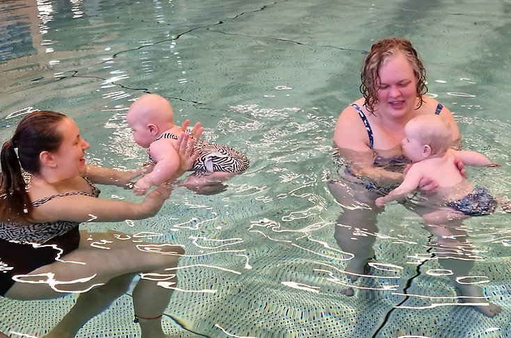 Två mammor håller i sina bebisar i vattnet.