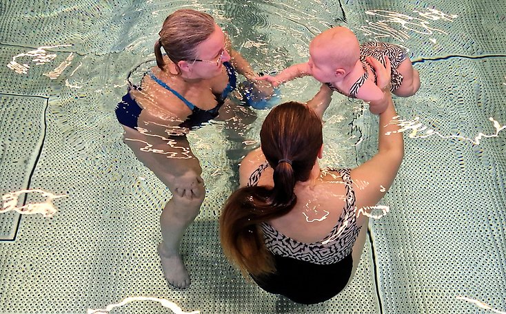 Två kvinnor och en bebis är i en bassäng.