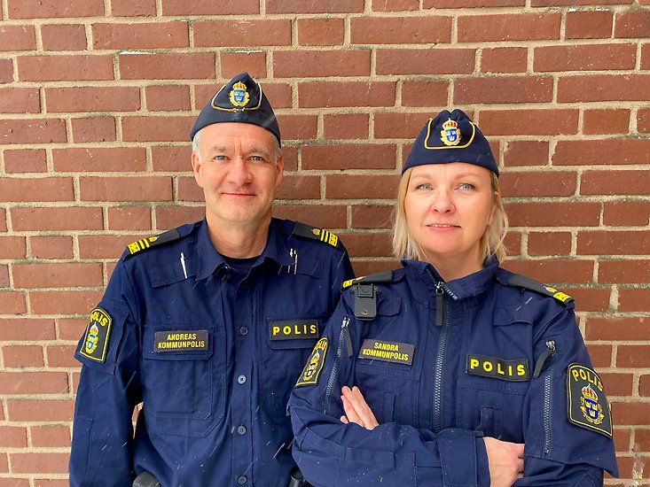 Två poliser står framför en tegelvägg.